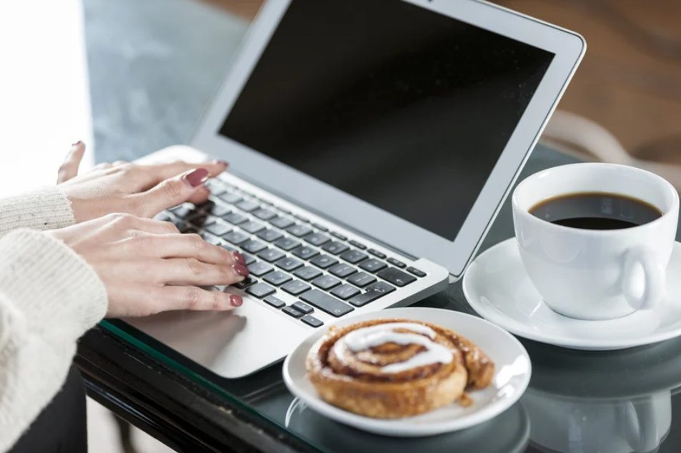 female hands typing at a computer with a coffee and pastry